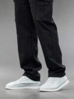 Man standing on a street wearing N Club black baggy cargo jeans with large flap cargo pockets on the thighs and a loose, comfortable fit